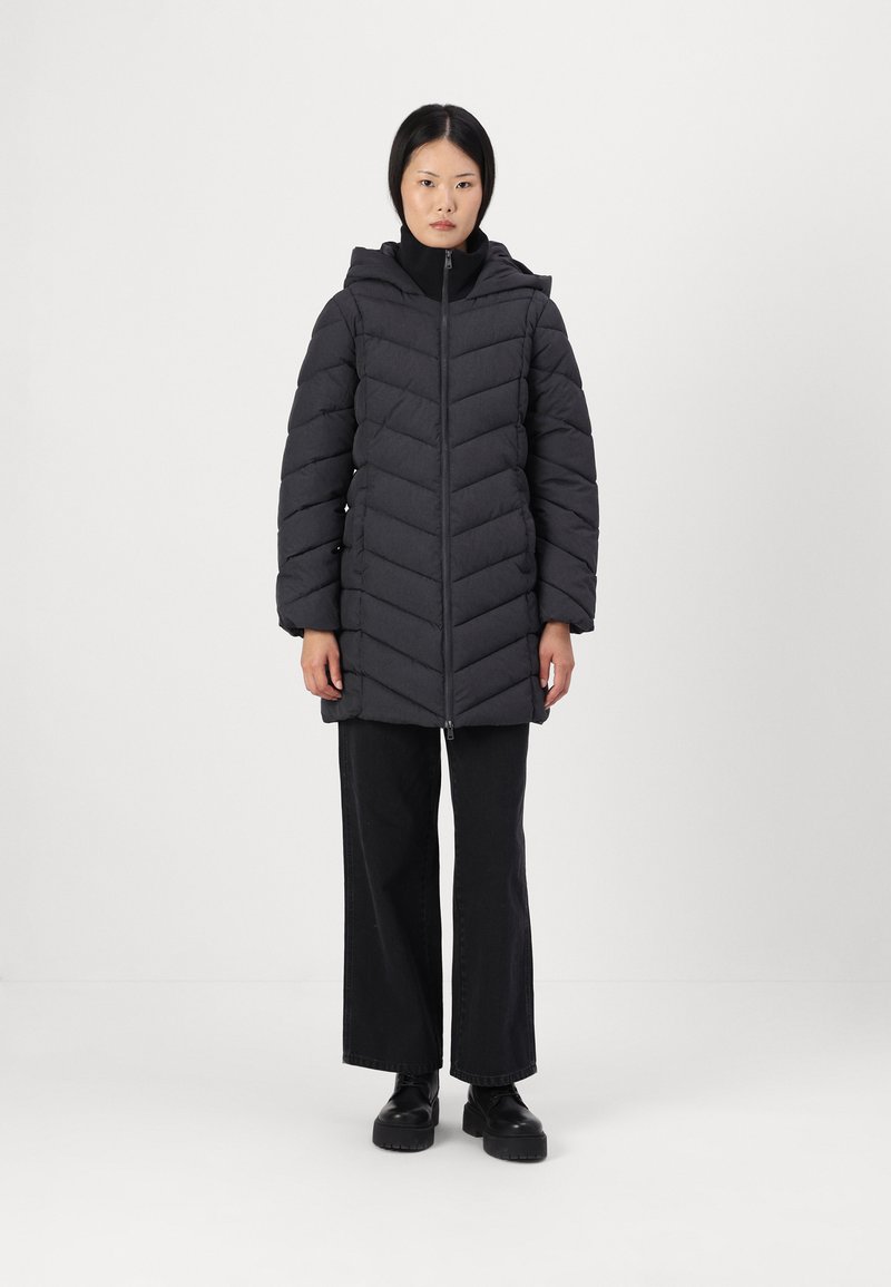 Zwarte pufferjack met een chevronpatroon, ritssluiting en capuchon. Draagt het over een zwart top, gecombineerd met brede zwarte broek, staan op een effen achtergrond.