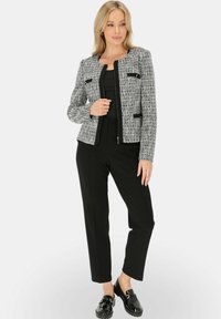 Szara marynarka z tweedu z czarnymi akcentami, zapinana na suwak z przodu, z czterema kwadratowymi kieszeniami. W zestawie z czarnymi, dopasowanymi spodniami i błyszczącymi butami.