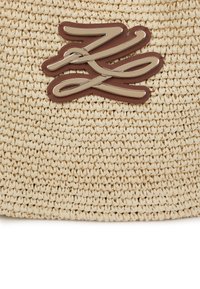 A természetes színű, szőtt szalma táska barna bőr logóval díszítve, kerek formával és texturált felülettel rendelkezik.