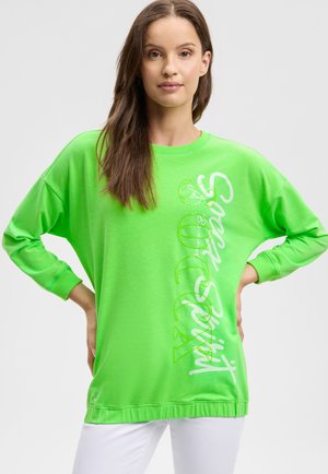 Helles grünes, übergroßes Sweatshirt mit langen Ärmeln, weißem Textgrafik auf der Seite sowie gerippten Bündchen und Saum.