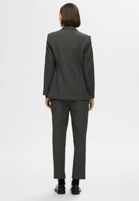 Costume sur mesure gris foncé avec un blazer structuré à revers et un pantalon slim fit, fabriqué dans un tissu lisse avec un léger éclat.