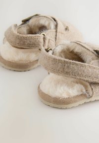 Chaussons en feutre beiges avec intérieur en peluche, straps en velcro et semelle texturée. Dispose d'un intérieur doux semblable à de la fourrure et d'un matériau durable.