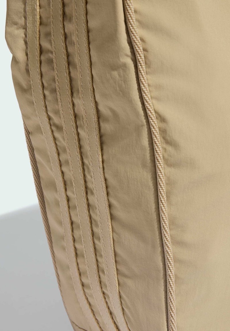 Beige Stofftasche mit vertikalen Nählinien und strukturierten Akzenten. Das Material wirkt glatt und hat ein leichtes Design.