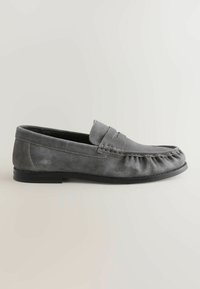Mocassin homme en daim gris avec couture mocassin, semelle noire plate et détail fente pour pièce sur un fond clair neutre.