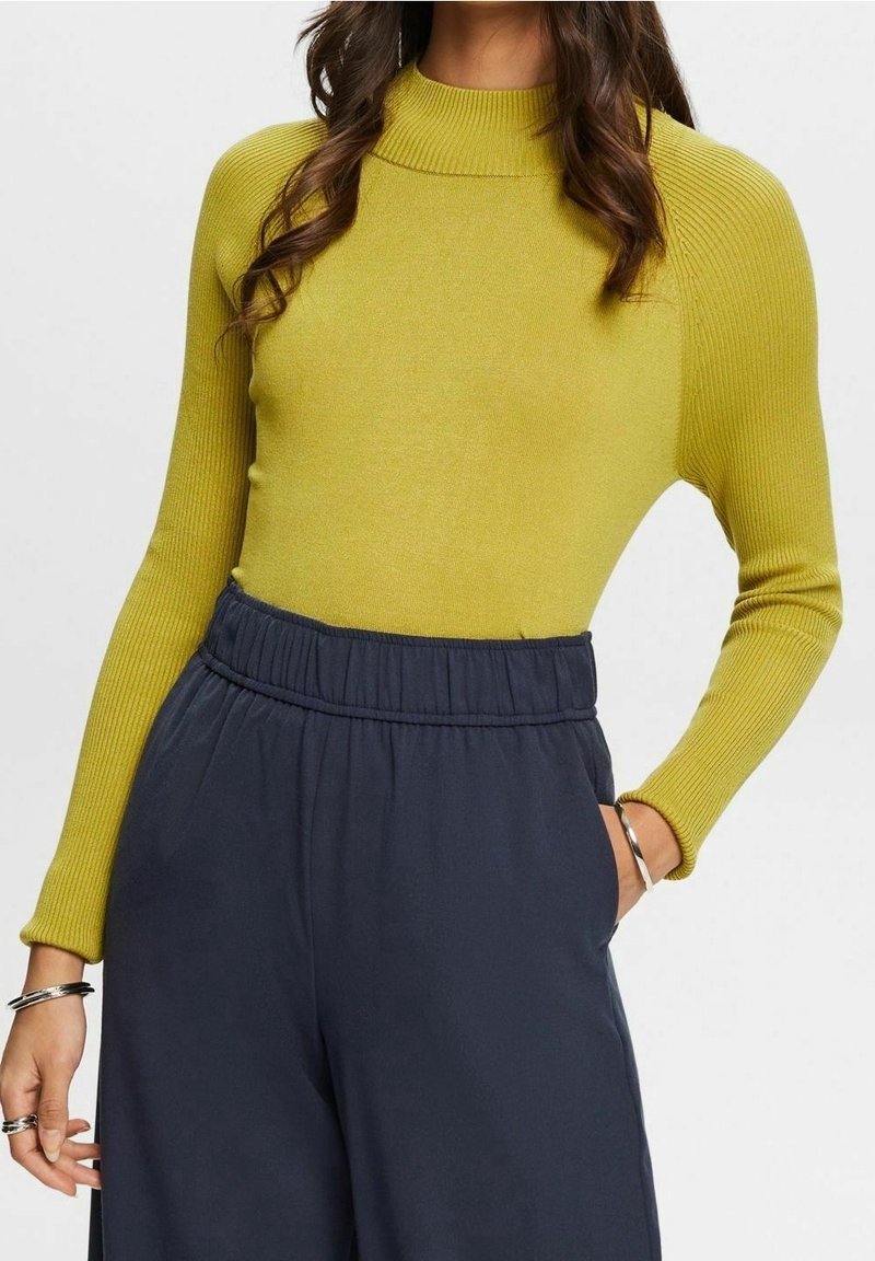 Haut à manches longues côtelé de couleur jaune vif, associé à un pantalon taille haute bleu marine avec une ceinture élastique et des poches latérales.
