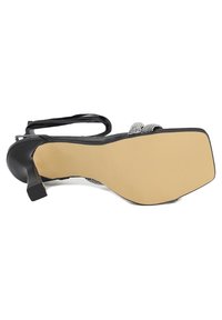 Scarpa nera con tacco alto, in pelle strutturata, con dettagli in strass trasparenti, cinturino alla caviglia e una suola in gomma liscia e di colore chiaro.