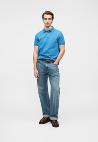 Polo bleu, jean bleu clair, ceinture marron, chaussures marron. Coupe décontractée ; design simple avec manches courtes et col.