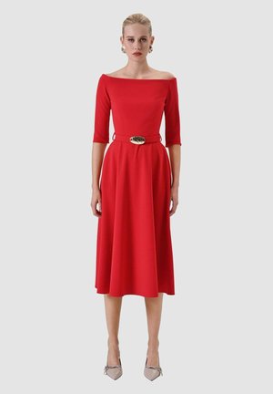 Abito rosso con scollo a barca, maniche tre quarti, cintura in vita con fibbia dorata e gonna svasata. Realizzato in tessuto liscio.