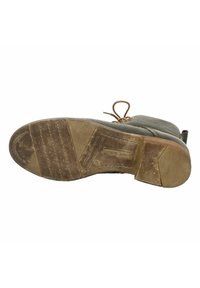 Botte en cuir marron avec une surface texturée, des lacets en haut et une semelle en caoutchouc montrant des signes d'usure, avec des lignes horizontales et un logo.