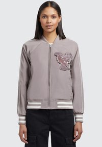 Veste bomber grise avec une fermeture éclair à l'avant et des poignets rayés. Présente un patch graphique de loup et une texture de tissu lisse. Coupe standard.