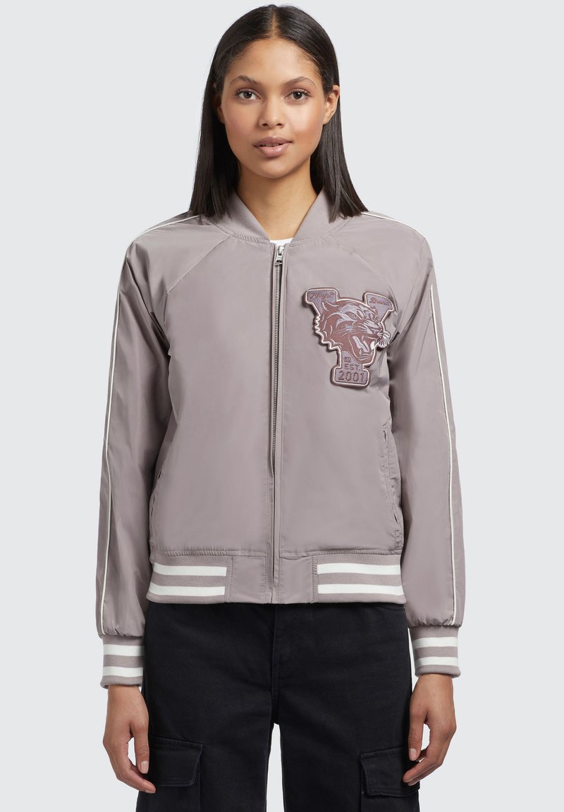 Veste bomber grise avec une fermeture éclair à l'avant et des poignets rayés. Présente un patch graphique de loup et une texture de tissu lisse. Coupe standard.
