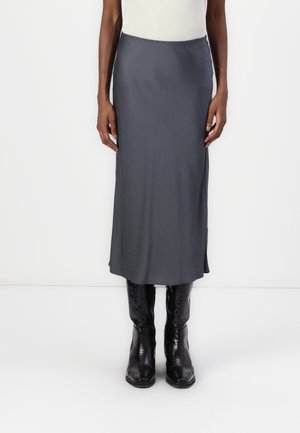 Person wearing a gray midi skirt and black textured leather boots, standing against a plain white background.