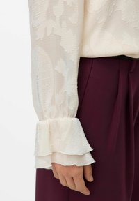 Valge tekstuuriga pluus koos kihiliste volangvarrukatega, kombineeritud burgundi värvi pükstega. Pluusil on kogu ulatuses keeruline muster.