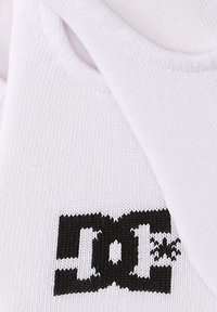 Weißer Stoff mit strukturierter Oberfläche, der ein auffälliges schwarzes Logo mit stilisierten Buchstaben "DC" und horizontalen Linien zeigt.