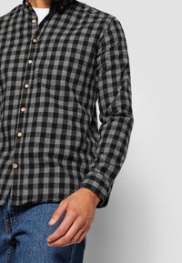 Camicia in flanella a scacchi nera e grigia con colletto a bottoni, caratterizzata da bottoni in legno e maniche lunghe. Indossata con jeans di denim blu.