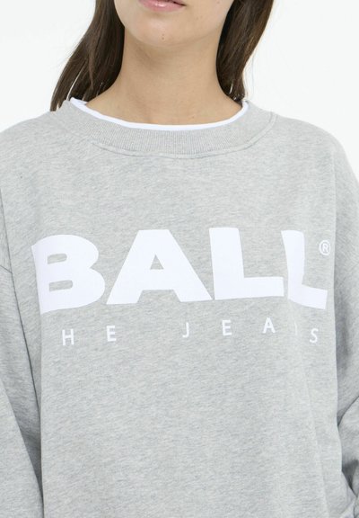 Sweatshirt gris avec un col rond, arborant un texte en gras, blanc, indiquant "BALL" et "THE JEANS" en dessous. Texture de tissu douce.