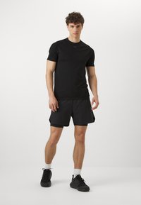 Camiseta atlética negra de manga corta con un corte ajustado, combinada con pantalones cortos negros. La tela parece ligera, adecuada para la actividad física.