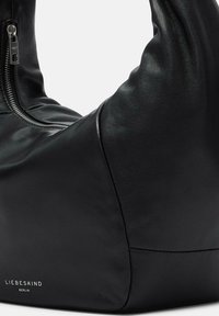 Czarna skórzana torba na ramię o zakrzywionym kształcie, gładkiej fakturze i srebrnym zamknięciu na zamek. Na boku widnieje logo "LIEBESKIND BERLIN".