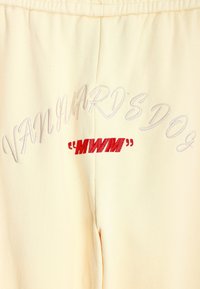 Tela de color crema que muestra texto bordado. "EL PERRO DE VANGUARDIA" en hilo claro, con "MWM" en negrita roja, centrado debajo. Textura suave, diseño casual.