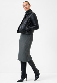 Schwarze Leder-Cropped-Jacke mit großen Knöpfen, kombiniert mit einem grauen, gerippten Strickrock und knielangen schwarzen Stilettos.