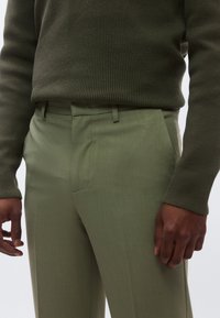 Olivengrøn ribstrikket sweater kombineret med matchende skræddersyede bukser med en glat tekstur og sidelommer.