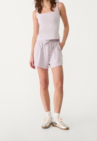 Top corto de lavanda claro con escote cuadrado y shorts a juego con cordón. Zapatos deportivos plateados con calcetines blancos completan el atuendo.