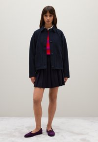 Navy blue, oversized wool jacket with front buttons and two pockets, paired with a pleated black skirt and purple flats. Smooth texture.