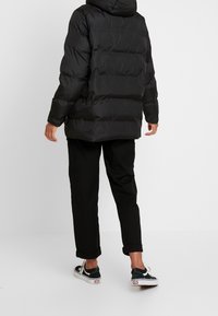 Sort polstret jakke med hætte, med vandret syninger og en afslappet pasform. Bæres med sorte bukser og lave sneakers.