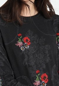 Pull noir avec broderie florale colorée comprenant des coquelicots rouges, de petites marguerites blanches et des accents verts. Texture douce, col rond.