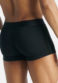 Svarta atletiska shorts med en slät yta, med en bred midja och diskreta sidostråk. Den figurnära designen förbättrar rörligheten.