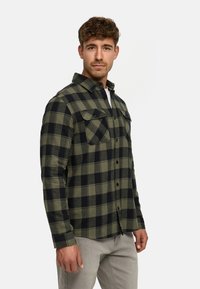 Camisa de franela a cuadros verdes y negros con dos bolsillos en el pecho y cierre de botones, material de algodón, diseño ligeramente ajustado.