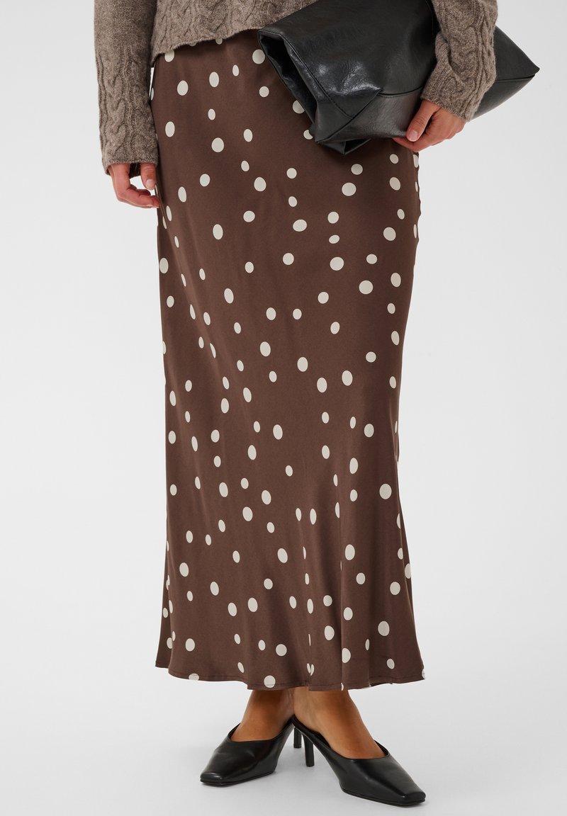 Jupe longue marron à pois blancs, portée avec des chaussures à talons noires, un pull marron et une pochette en cuir noir.