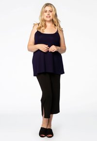 Donkerblauwe mouwloze top met een losse pasvorm, gecombineerd met zwarte cropped broek met zijslits, en zwarte open teen schoenen.