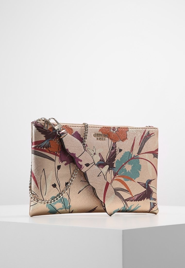 Petit sac pochette beige avec imprimés floraux et d'oiseaux colorés, chaîne argentée et logo "GUESS 1981" sur le devant.