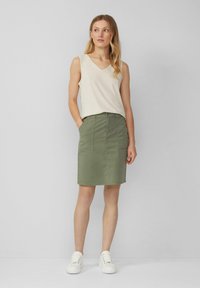 Haut sans manches beige clair, décolleté en V ; jupe olive à longueur genou avec poches avant, texture lisse et design simple ; baskets blanches.