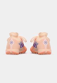 Różowe buty sportowe o strukturalnym wzorze, elastycznym kołnierzu, fioletowych akcentach i podeszwie z kolcami zapewniającymi przyczepność. Widoczne logo po bokach.