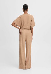 Beige, lockere Overall aus strukturiertem Stoff. Kurze Ärmel, weite Beine und ein elastischer Bund sorgen für eine entspannte Silhouette.