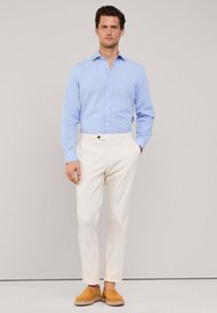 Camisa de botón azul claro, pantalones blancos ajustados y zapatos slip-on de ante beige. Diseño ajustado, textura suave y estilo minimalista.