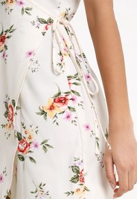 Květinové šaty z lehkého materiálu; mají krémové pozadí s růžovými, červenými a žlutými květy. Boční zavazování a splývavý střih.
