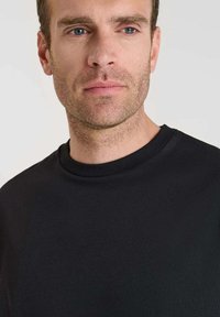 Pullover nero a collo rotondo realizzato in tessuto morbido. Presenta un design semplice senza motivi o loghi visibili, aderente intorno al collo.
