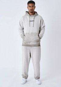 Lichtgrijze hoodie met trekkoorden en een voorzak, gecombineerd met bijpassende trainingsbroek en witte sneakers. Zachte stof met een relaxte pasvorm.
