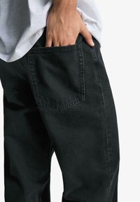 Sorte denimbukser med fem lommer og synlige syninger. Stoffet ser robust ud med en let struktur.