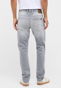 Szürke farmernadrág slim fit szabással, lapos derékkal, hátsó zsebek ívelt formával és egy textúrált bőr címkével a hátsó részen.