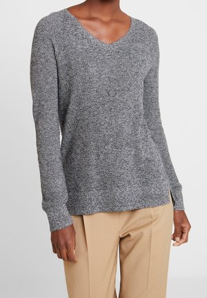 Pull en tricot gris à motif chevrons avec un col en V, des manches longues et des fentes sur les côtés, associé à un pantalon beige. Tissu texturé pour la chaleur et le confort.
