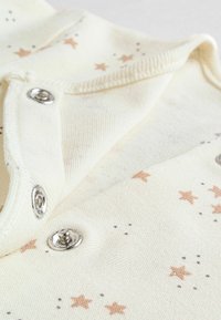 Tissu couleur crème avec un motif d'étoiles et de pois en rose et gris. Comprend des fermetures à pression en métal et une texture douce.