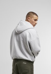 Grau Hoodie mit geräumiger Kapuze, gerippten Bündchen und lockerer Passform, kombiniert mit dunkelgrünen Hosen, die auf der Tasche eine gestickte Markenbezeichnung aufweisen.