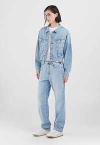 Lyseblå denimjakke med to brystlommer, kombinert med matchende lyseblå jeans. Hvit t-skjorte under og hvite joggesko.