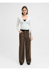 Bela zgornja obleka z dolgimi rokavi, kombinirana z rjavimi širokimi hlačami z vzorcem kačje kože, oboje oblečeno s črno obutvijo.