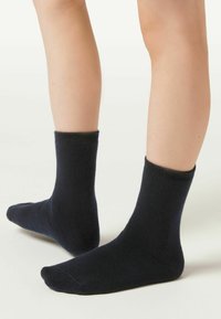 Marinblå bomuldsstrømper med ribbet tekstur, crew-længde design og subtile hæl- og tådetaljer. Glat overflade og tætsiddende pasform.