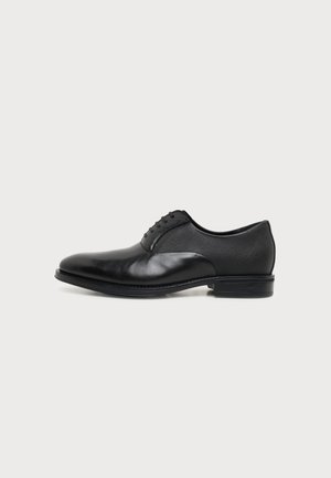 Chaussure habillée pour homme en cuir noir à lacets, talon bas et bout lisse, vue de profil sur un fond clair uni.